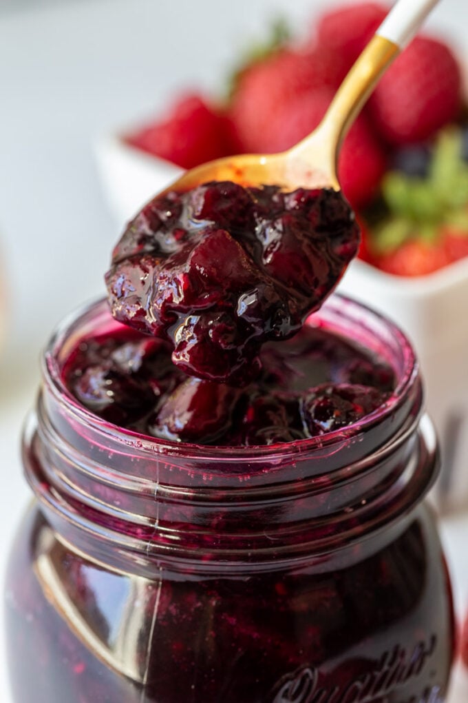 spoon dishing out berry sauce from a mason jar