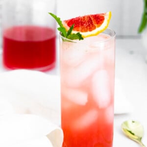 Tall glass filled with ice and a blood orange mojito and blood orange slice and mint on the top