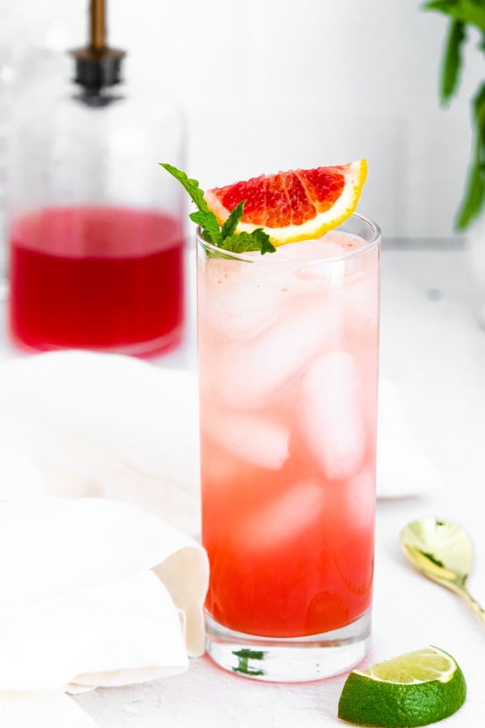 Tall glass filled with ice and a blood orange mojito and blood orange slice and mint on the top