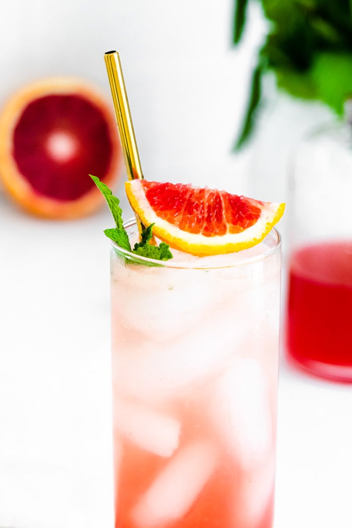 up close shot of Tall glass filled with ice and a blood orange mojito and blood orange slice and mint on the top
