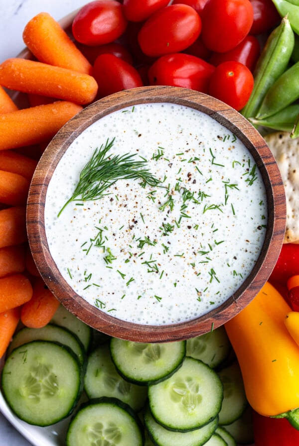 cottage cheese ranch in a wood bowl topped with fresh dill. The bowl is surrounded by fresh colorful veggies and crackers
