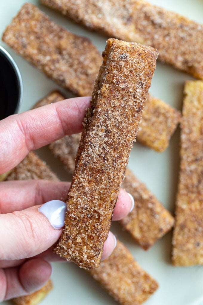 Hand holding a cinnamon sugar French toast stick.