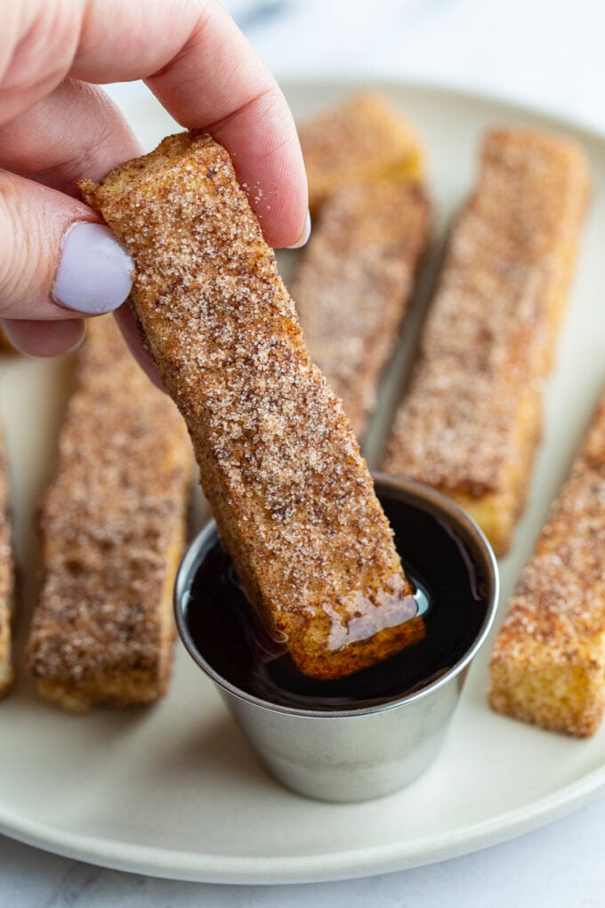 Woman's hand dipping a French toast stick into maple syrup.