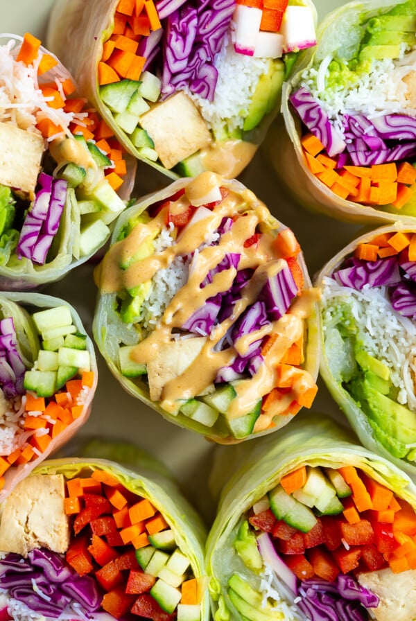 giant summer rolls stuffed with cabbage, radish, avocado, bell pepper, cucumber, tofu, and carrot. they're cut in half so you can see everything inside. One of the rolls is drizzled with peanut sauce