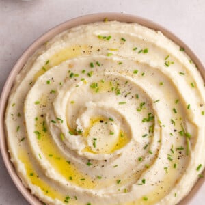 mashed potatoes swirled into a pink dish and topped with chives. bowl of chives in the corner