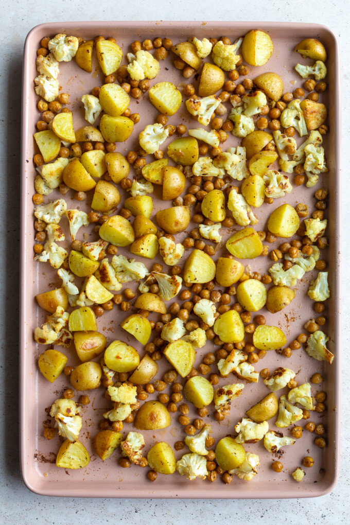 light pink sheet pan with roasted veggies on it: chickpeas, cauliflower, and potatoes