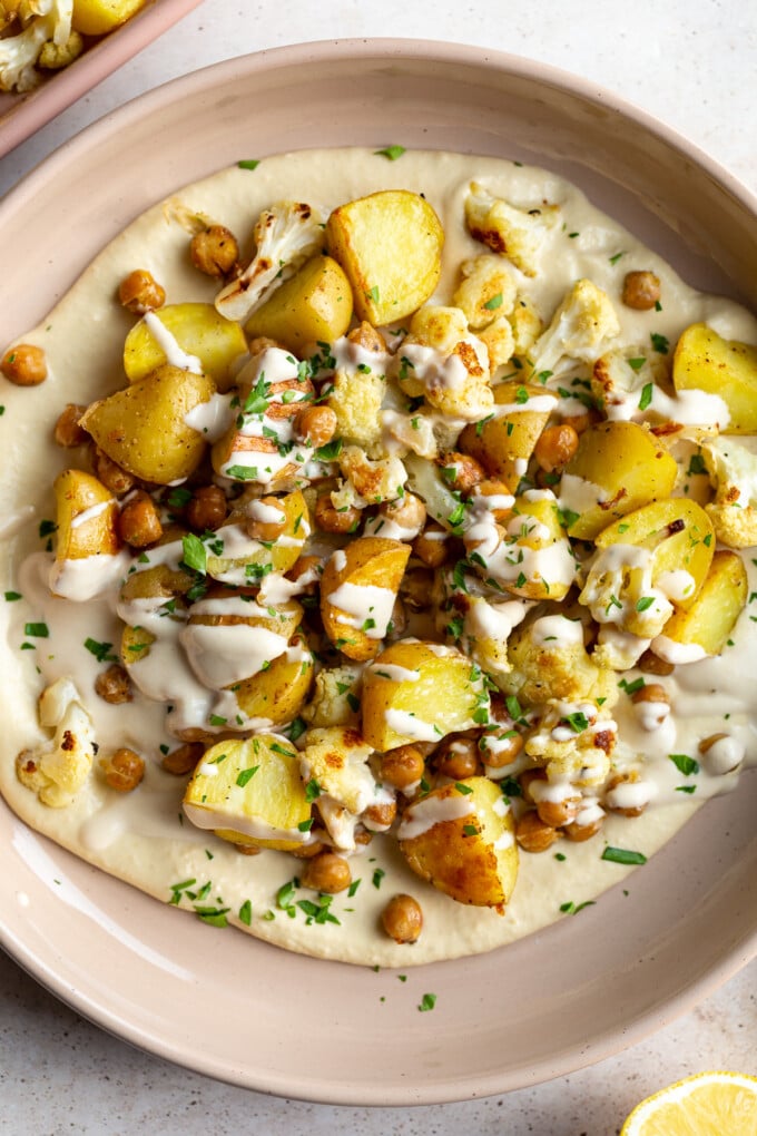 veggie bowl with roasted potato, chickpeas and cauliflower on a bed of creamy hummus and drizzled with a white tahini sauce