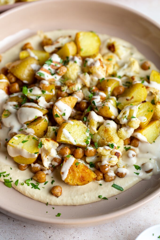 veggie bowl with roasted potato, chickpeas and cauliflower on a bed of creamy hummus and drizzled with a white tahini sauce