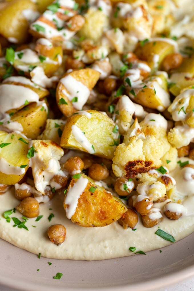 veggie bowl with roasted potato, chickpeas and cauliflower on a bed of creamy hummus and drizzled with a white tahini sauce
