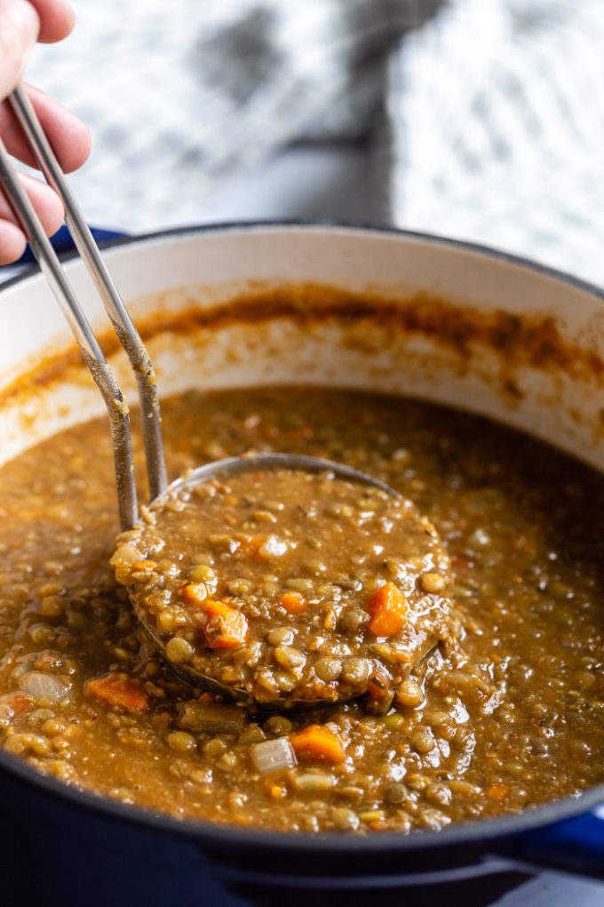 large pot of vegan lentil soup with veggies. a ladle is dipping into the pot to pull up a scoop full of the soup