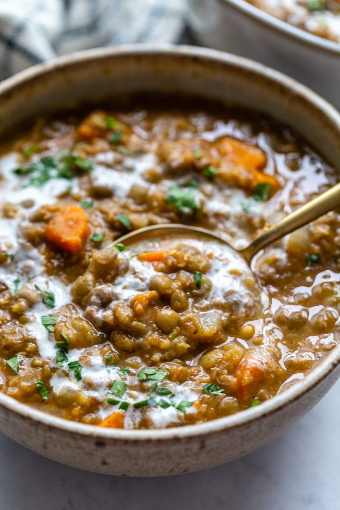 up close shot of a bowl of brown lentil soup with carrots in it and a spoon coming out the side