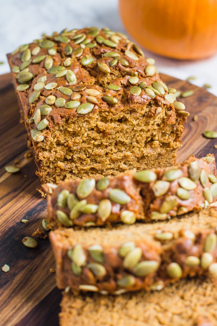 vegan pumpkin bread cut open with pepitas baked on top and a pumpkin in the background
