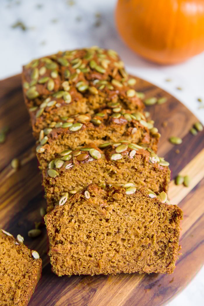 vegan pumpkin bread cut open with pepitas baked on top and a pumpkin in the background